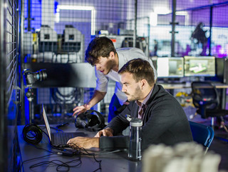 Two men leaning over a computer surrounded by VR and robotics equipment