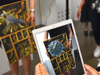 A student holding an iPad in front of a physical drawing showing an augmented reality feature on the screen