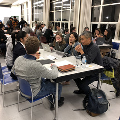 Image of students gather around a table with a professional sharing feedback on their portfolios