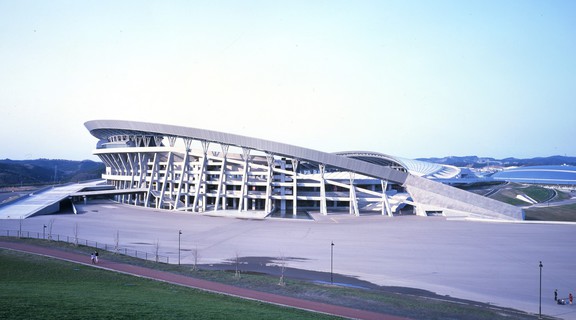 Exterior shot of Miyagi Stadium, a white curved building based on concentric circles in a park-like setting in Sendai, Japan.