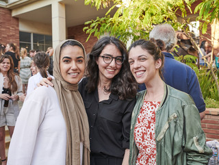 Three female students smiling in front of a group of people