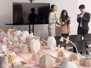 Two female students looking down at a model in a large warehouse space lit with purple lighting