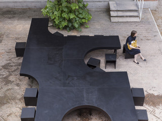 Image of the Leong Leong submission for the Venice Biennale XIV, a black table/bench structure shown with a woman sitting in the foreground