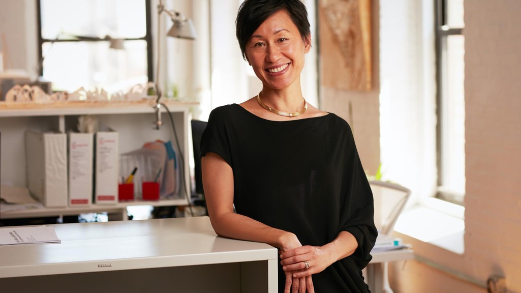 A photograph of a woman leaning on a work table, with models of buildings in the background