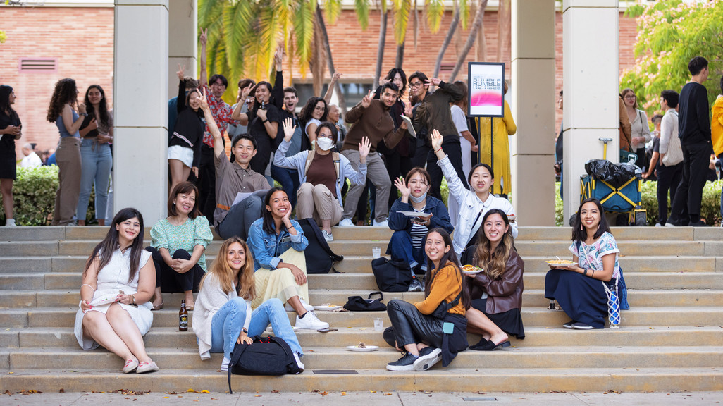 a photograph of people sitting on a staircase with palm trees and pillars in the background