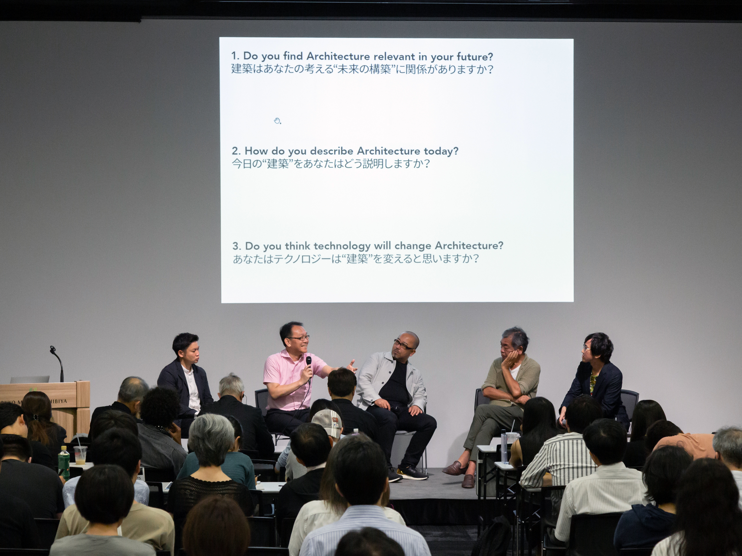 A panel of five people sitting in front of a screen with English and Japanese text