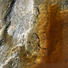 Aerial photograph of dried lake bed with white and tan coloration on the left side that fades to brown in the middle and rusty clouded tones on the right.