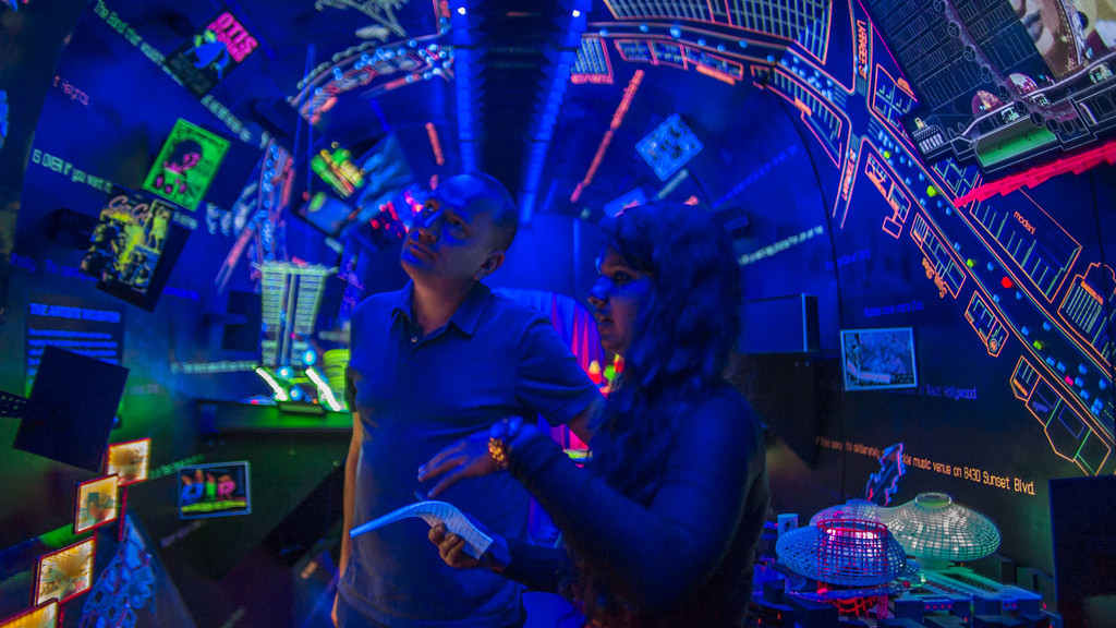 Two people inside the immersive SUNSET 2050 exhibition, lit with blue and fluorescent light